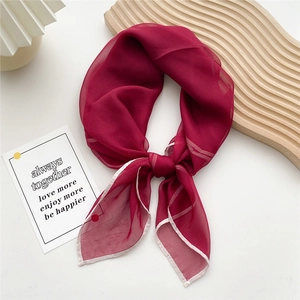 Elegant deep red sheer square silk scarf with white stitched edges on a wooden surface