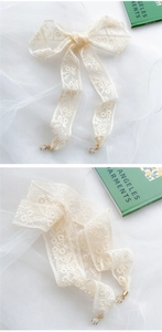Detail eines cremefarbenen Spitzenbandes mit Blumenstickerei und goldenem Karabiner
