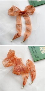 Detail einer orangefarbenen floralen Spitzenschleife mit Goldring und Perlenanhänger