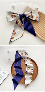 Close-up of narrow silk scarf with navy cherry patterns and elegant orange typography