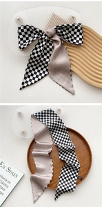 Close-up of checkerboard and champagne satin skinny scarf tied in a bow on a wooden tray