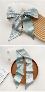 Detailed close-up of light mint silk scarf with coral patterns and elegant typography