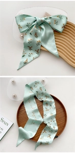 Close-up of mint green satin silk scarf with orange floral and cursive text details