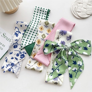 Elegant floral and polka dot skinny silk scarves tied in bows on a minimalist white desk