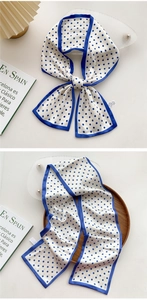 Detailed view of a white silk scarf with blue polka dots and a wide blue border trim
