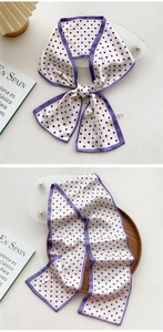 Detail of a purple polka dot narrow silk scarf tied as a bow on a minimalist background