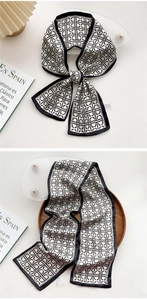 Detail of a black and white geometric silk twilly scarf tied on a luxury wooden tray