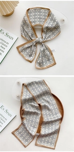 Close-up of beige silk scarf with grey geometric patterns and brown borders on wooden tray