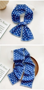 Close-up of a blue silk scarf with white monogram patterns and gray piped edges