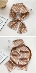Detail of satin skinny scarf with 'C' letter print and smooth texture on wooden tray