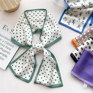 Elegant white silk scarf with green polka dots tied in a bow on a minimalist desk