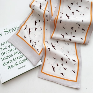 Elegant skinny silk scarf with bird print and orange border on minimalist book