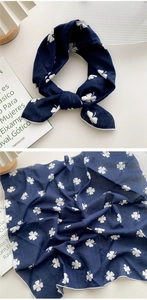 Détail d'un foulard bleu foncé à motif trèfle, présenté noué et à plat sur un bureau