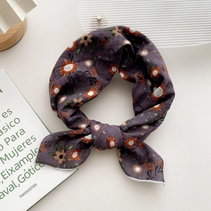 Foulard carré en lin à fleurs violettes noué en nœud sur un bureau blanc