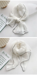 Detail view of thin white chiffon scarf with black stitched edges tied in a bow