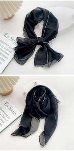 Detail of a thin black translucent scarf featuring white lettuce edge trim and bow styling
