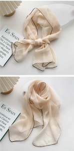 Detail of a beige long silk scarf with black wavy edges draped on minimalist decor