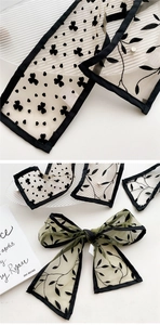Detail of sheer mesh scarf featuring black flocked floral and clover patterns