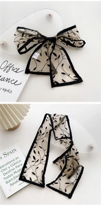 Detail of a sheer beige mesh hair ribbon with black leaf patterns and silk satin piping