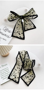 Detail of light green chiffon scarf with black leaf print tied into a stylish bow