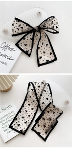 Close-up of narrow white silk scarf with black clover print and elegant bow styling