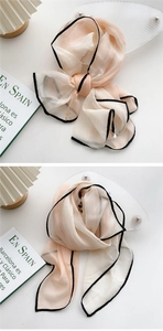 Detail of light beige chiffon scarf with black piping edges on a decorative setup