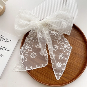 Elegant white lace bow hair clip with floral embroidery and long ribbons on wooden tray