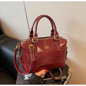 Macro detail of deep red leather Boston bag featuring white stitching and gold hardware
