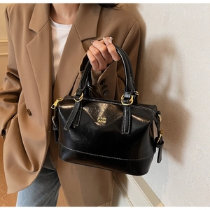 Macro shot of black glossy leather Boston bag featuring gold hardware and logo detail