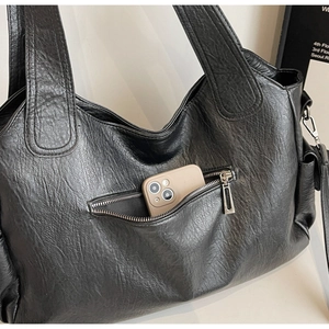 Detail of black dumpling bag with lychee texture and phone in silver zipper pocket