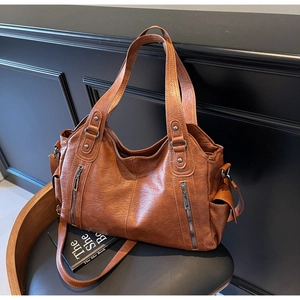Detail of vintage brown leather tote bag with vertical metal zippers on a dark chair