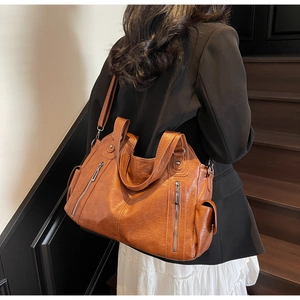 Macro detail of brown leather tote bag showing vintage textures and zipper pockets