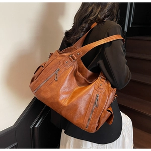Detail view of brown leather tote bag showing multiple zipper pockets on a model