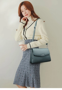 Detail of dark green lychee leather handbag with silver logo on beige cardigan outfit