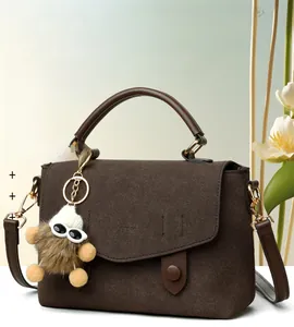 Detail of dark brown faux suede messenger bag with gold hardware and plush charm