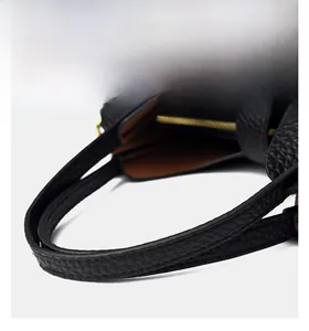 Detail of black lychee leather handbag handle with reinforced stitching and gold ring