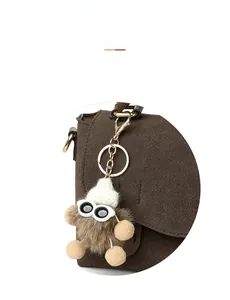 Detail of cute brown plush monster charm with tiny glasses on a brown messenger bag