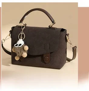 Detail of dark brown suede messenger bag with gold hardware and plush bear charm