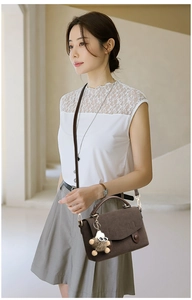 Detail of a large brown suede messenger bag with a cute bear charm on a model