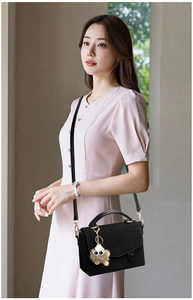 Close-up of black leather messenger bag with gold hardware and plush doll pendant