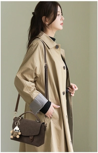 Detail of dark brown suede messenger bag with plush charm on a khaki trench coat