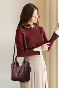Detail of dark purple lychee grain leather bucket bag with teddy bear charm on model