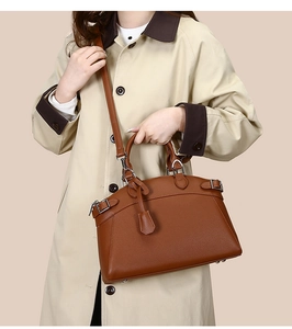 Brown litchi leather tote bag with round handles worn by a model in a trench coat
