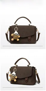 Detail of dark brown matte messenger bag with top handle and plush monster charm