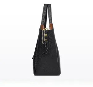 Detail view of black litchi grain leather bucket bag with gold chain and bear pendant