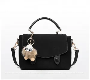 Detail of black suede messenger bag with gold hardware and plush monster charm