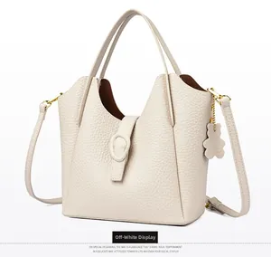 Close-up of beige lychee grain leather bucket bag with cute bear charm and gold hardware