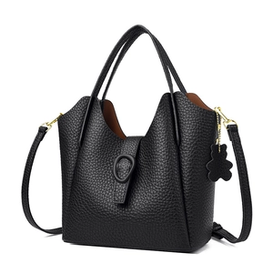 Black pebbled leather bucket bag with top handles, crossbody strap and bear charm decoration