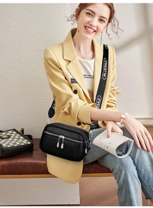 Close-up of a black textured leather crossbody bag with triple zippers and wide strap