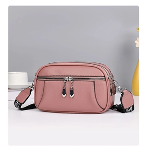 Detail view of pink leather crossbody bag with three zipper compartments and wide strap
